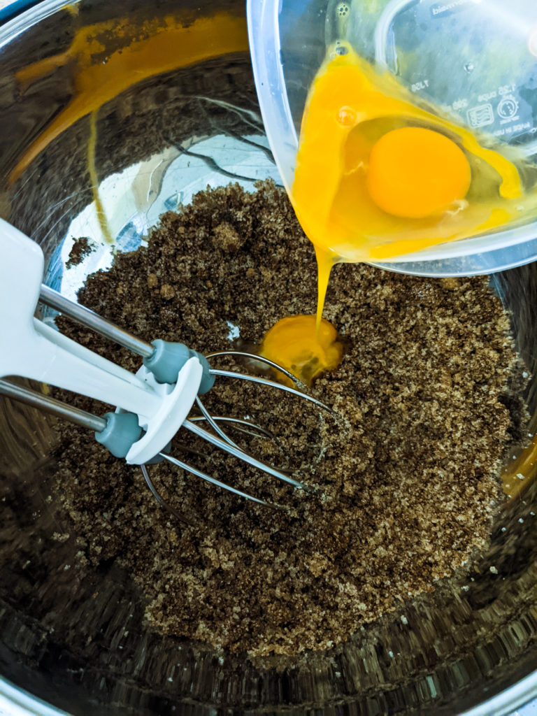 large egg and egg yolk being poured into a bowl of wet ingredients