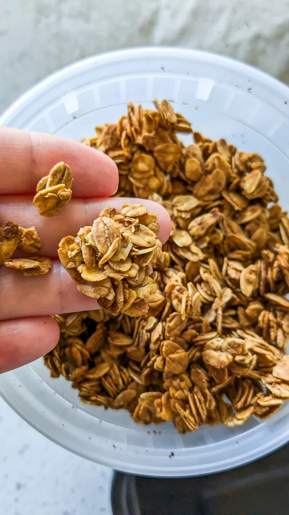 granola in a hand above a container of granola